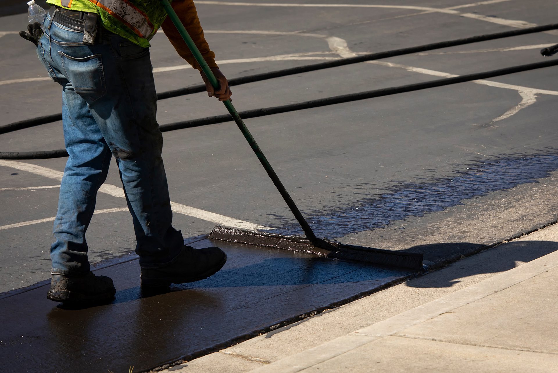 Worker using a sealcoating brush during asphalt resurfacing project